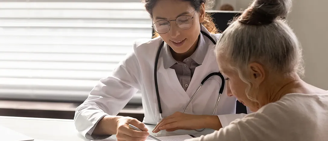 Female doctor in a white coat discussing paperwork with an elderly woman in a medical office.