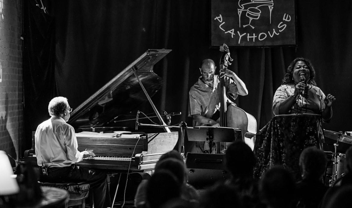 A jazz trio performs on stage in a cozy venue called "Playhouse."