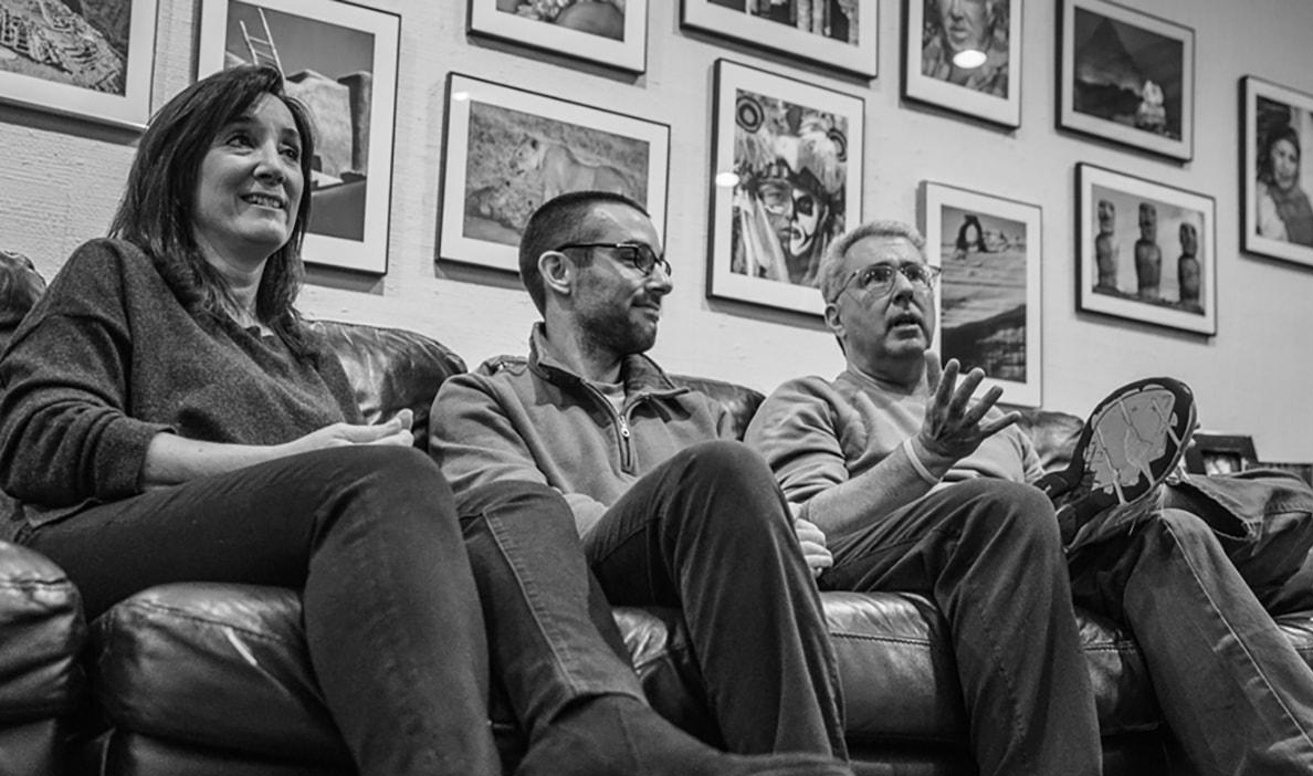 Three people sit on a leather couch engaged in a conversation.