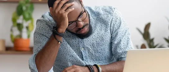 Worried man sitting at a desk with his head resting on his hand, looking at financial documents.