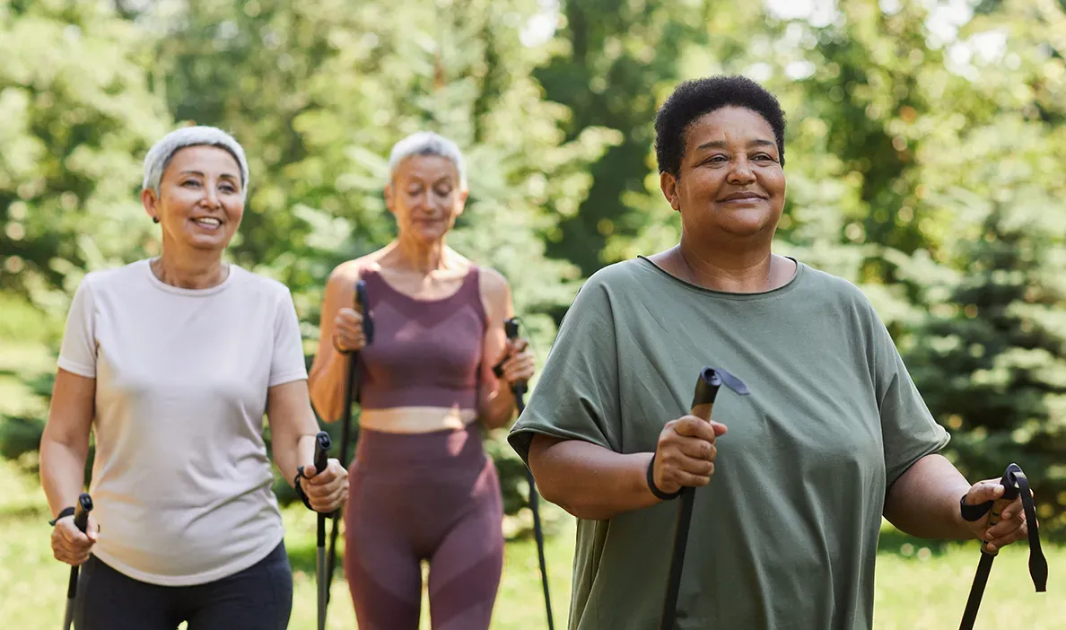 Three women engaging in Nordic walking outdoors, smiling and enjoying a fitness activity in nature.