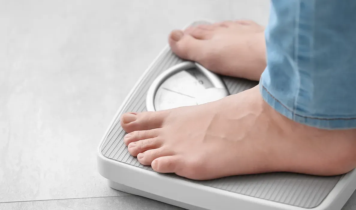 Person standing on a weighing scale, focusing on their feet and the scale's dial.