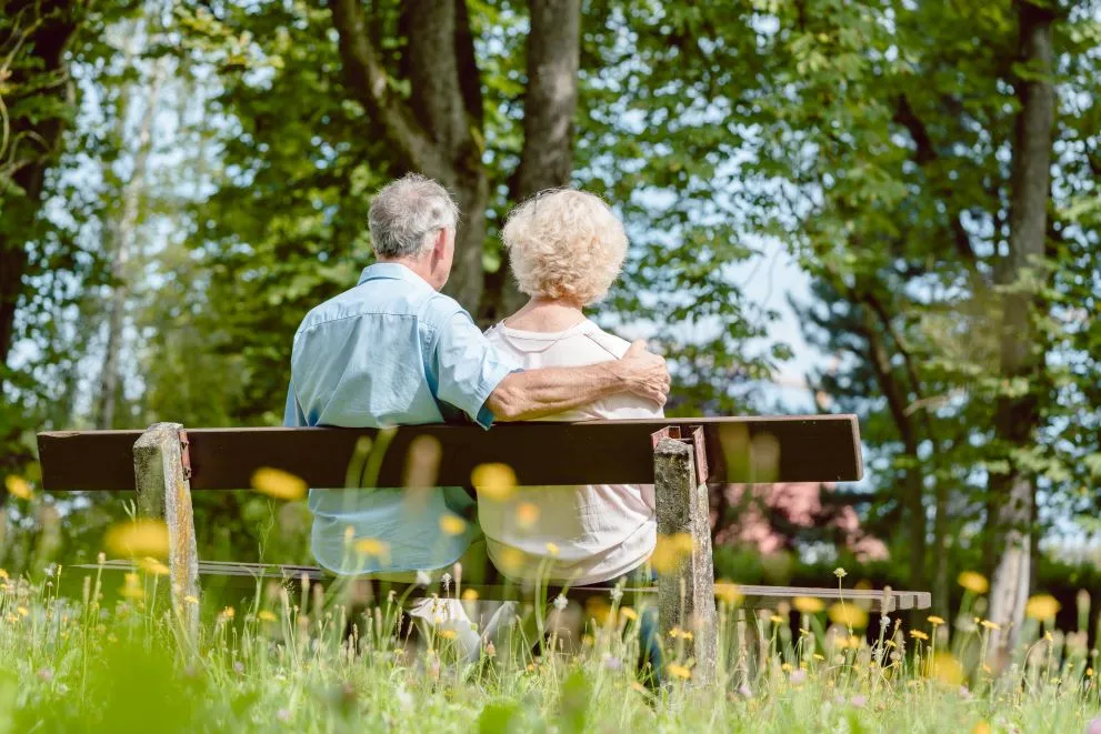 A couple sat on a bench, the man with his arm around the lady