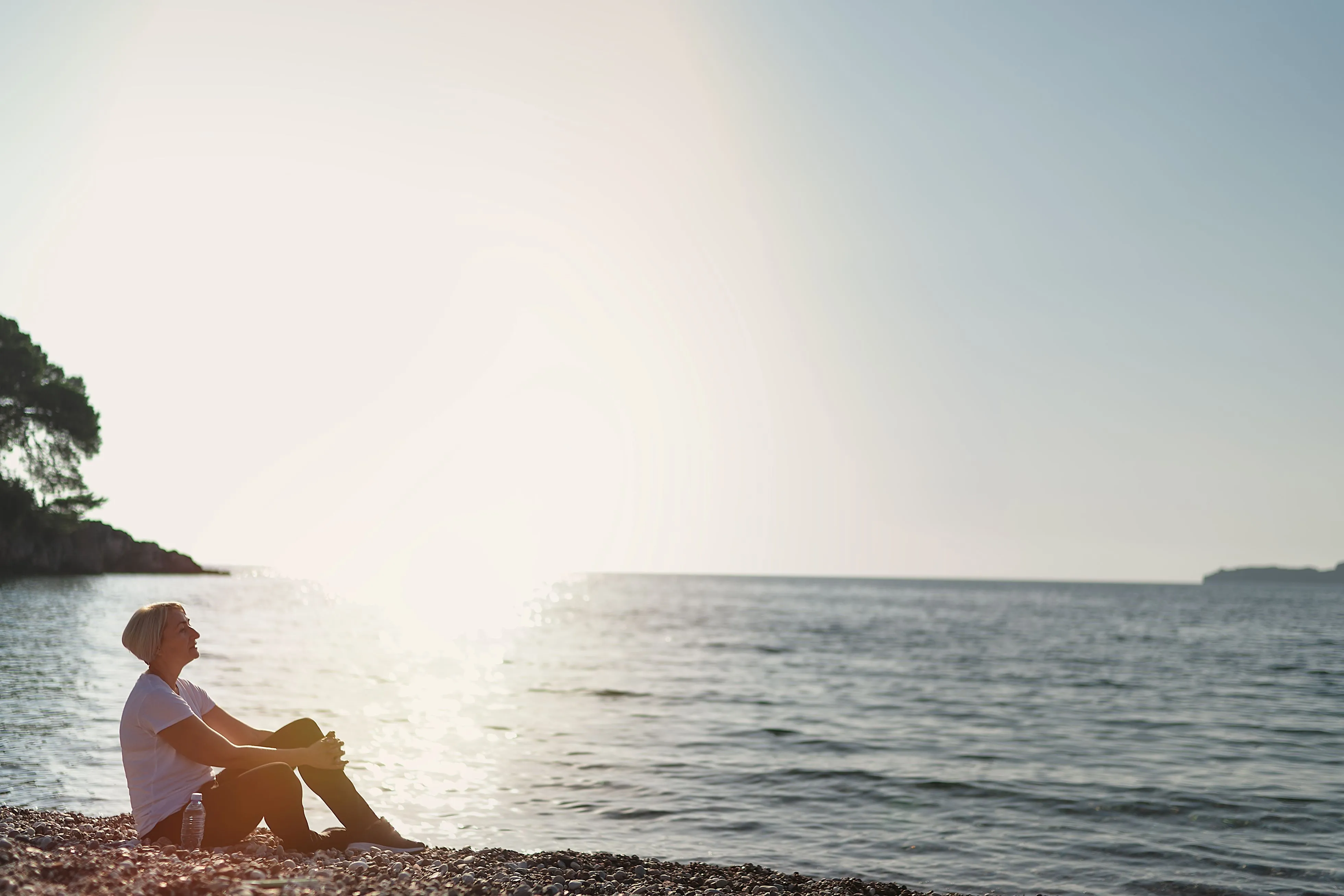 woman sitting on the beach with the sun shining behind 