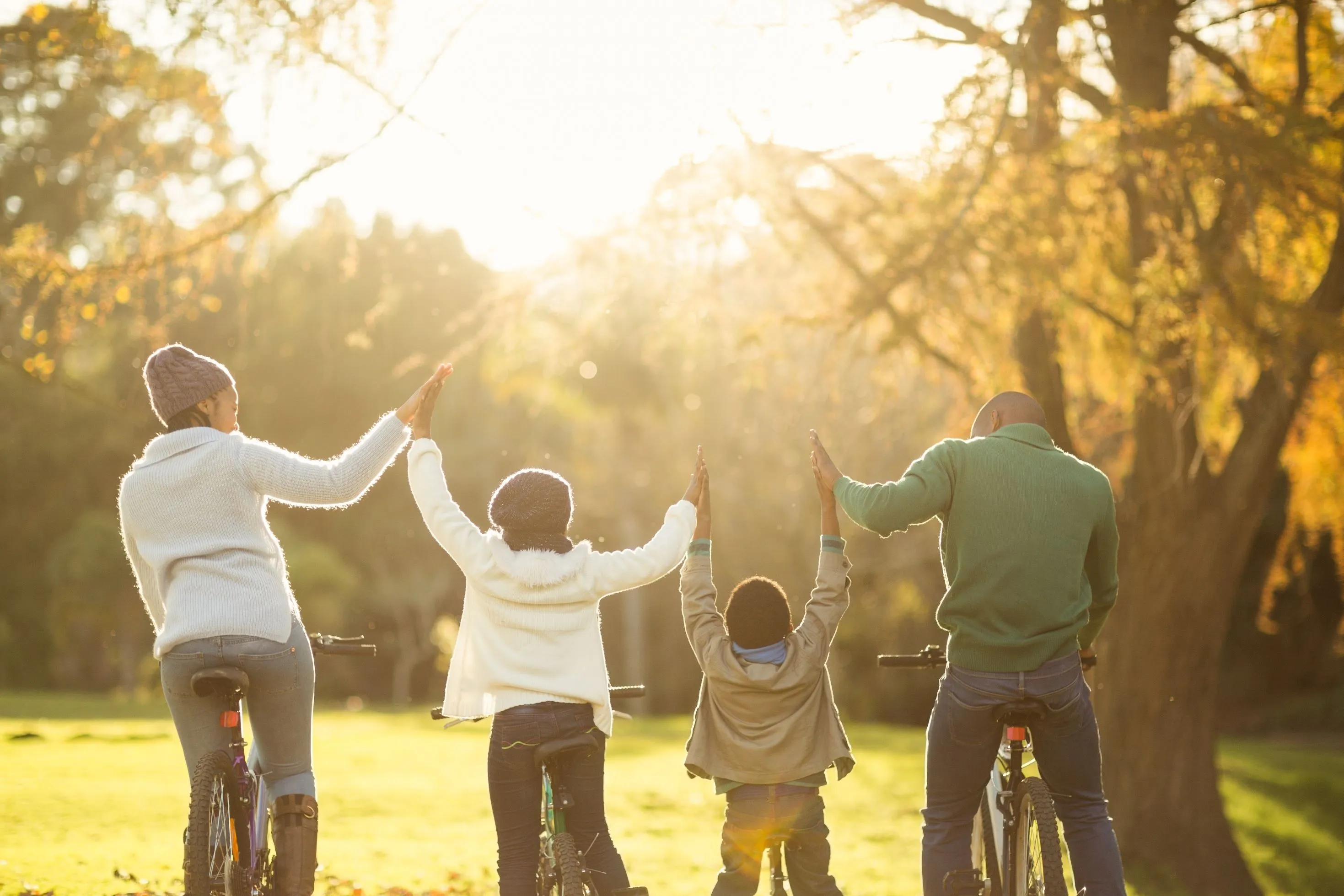 a mother, father and two children holding hands and riding bicycles on a field surrounded by trees 