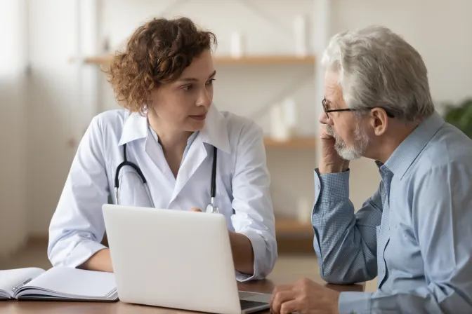 Healthcare professional and an older patient having a conversation and looking at a laptop 