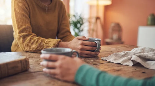 Two people holding mugs at a wooden table in a cosy, softly lit room