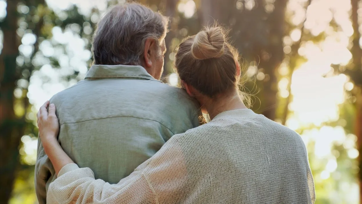 Two people walking outdoors with their arms around each other