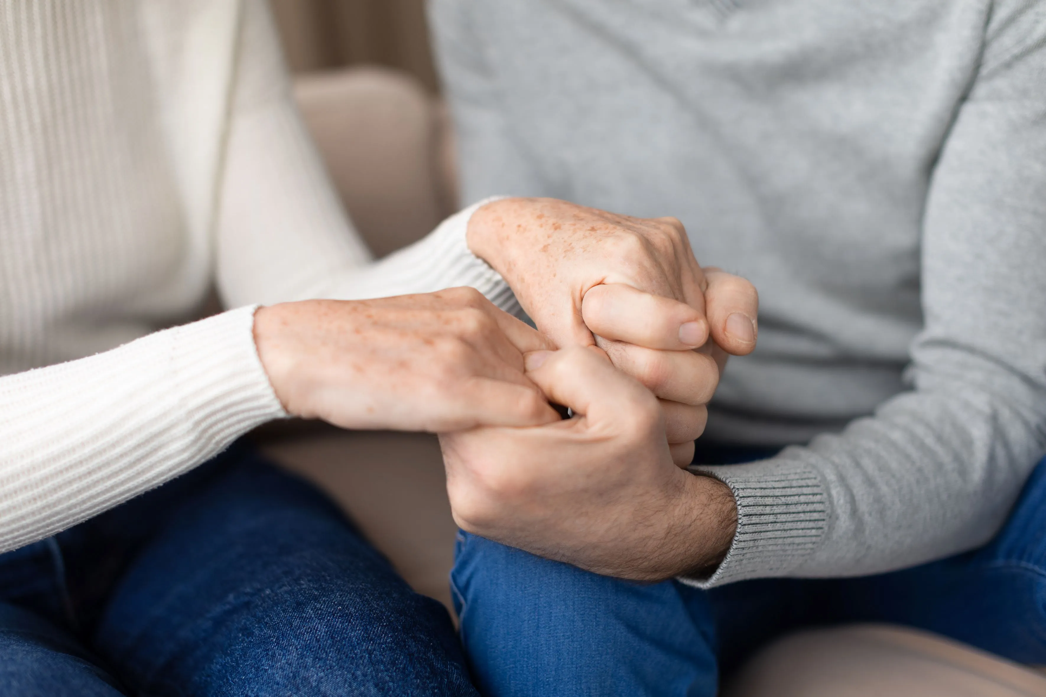 Close-up of two people holding hands in a supportive gesture while seated together