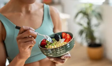 Alt text: A person wearing a white linen shirt holds a ceramic bowl filled with a colorful salad, including chickpeas, red bell peppers, shredded carrots, green beans, and seeds.