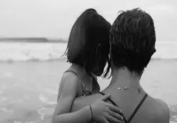 A black and white photo of a woman standing in the ocean, holding a young girl in her arms.