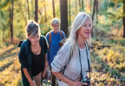 Group of women hiking in the forest, smiling and enjoying the fresh air while carrying backpacks.