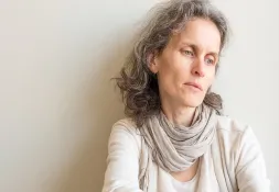 woman sitting on a couch, resting her chin on her hands, looking thoughtful and concerned.