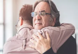 Older man with glasses embracing a younger man, eyes closed, showing an emotional and heartfelt moment.