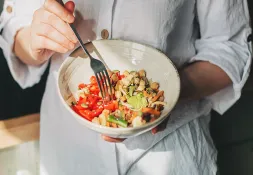 Person in a white shirt holding a bowl of colorful, nutrient-rich food, including chickpeas, vegetables, and seeds.