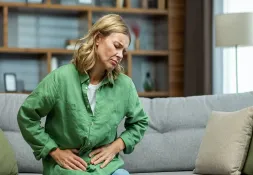 Woman sitting on a couch, holding her stomach with a displeased expression. A representation of sensitivity to smells.