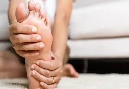 Person holding their foot with both hands, possibly experiencing pain or numbness. A visual representation of peripheral neuropathy, a common side effect of cancer treatment.