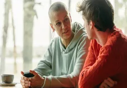 Woman with a shaved head wearing a hoodie having a serious conversation with a man in a café.