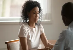 Woman with curly hair sitting at a table, having a serious conversation with a man.