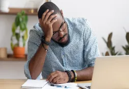 Worried man sitting at a desk with his head resting on his hand, looking at financial documents.