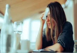 Woman sitting at a table, wiping sweat from her forehead with a tissue.