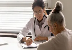 Female doctor in a white coat discussing paperwork with an elderly woman in a medical office.