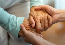 Close-up of a younger person gently holding the hands of an elderly person, symbolising care, support, and compassion.