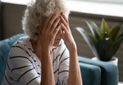 Woman sitting on a couch with her face in her hands.