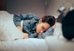 Young woman lying in bed, looking exhausted and deep in thought.
