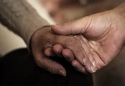A close-up of two hands, one frail and aged, gently held by a stronger, younger hand.