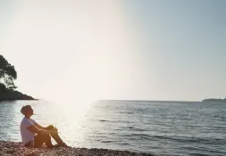 woman sitting on the beach with the sun shining behind 