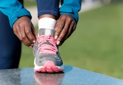 a woman tying her shoelaces wearing a grey show with pink laces and sporty clothes 