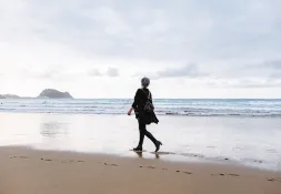 older woman walking along a beach alone 