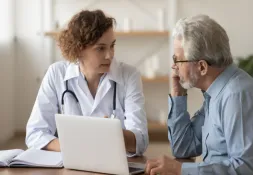Healthcare professional and an older patient having a conversation and looking at a laptop 