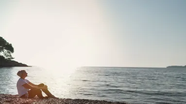 woman sitting on the beach with the sun shining behind 