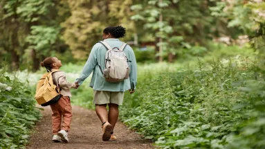 Woman and her child holding hands and walking along a path through a forest