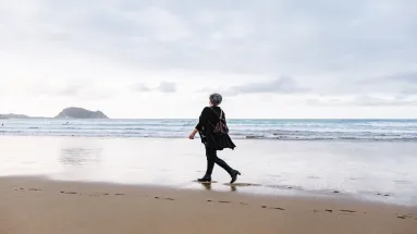 older woman walking along a beach alone 